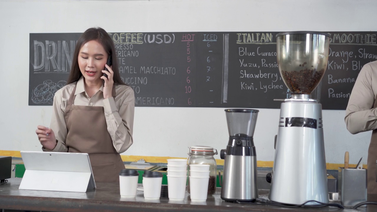 亚洲女性职员在咖啡店用智能手机与顾客交谈。视频素材