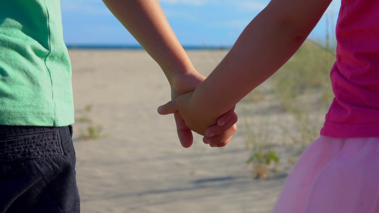 一个穿着粉色裙子的小男孩和小女孩在沙滩上手牵着手的特写视频下载