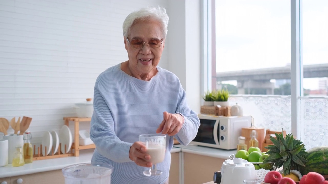 奶奶拿着混合果汁在手机上像上网一样和她的家人聊天或交流。视频素材