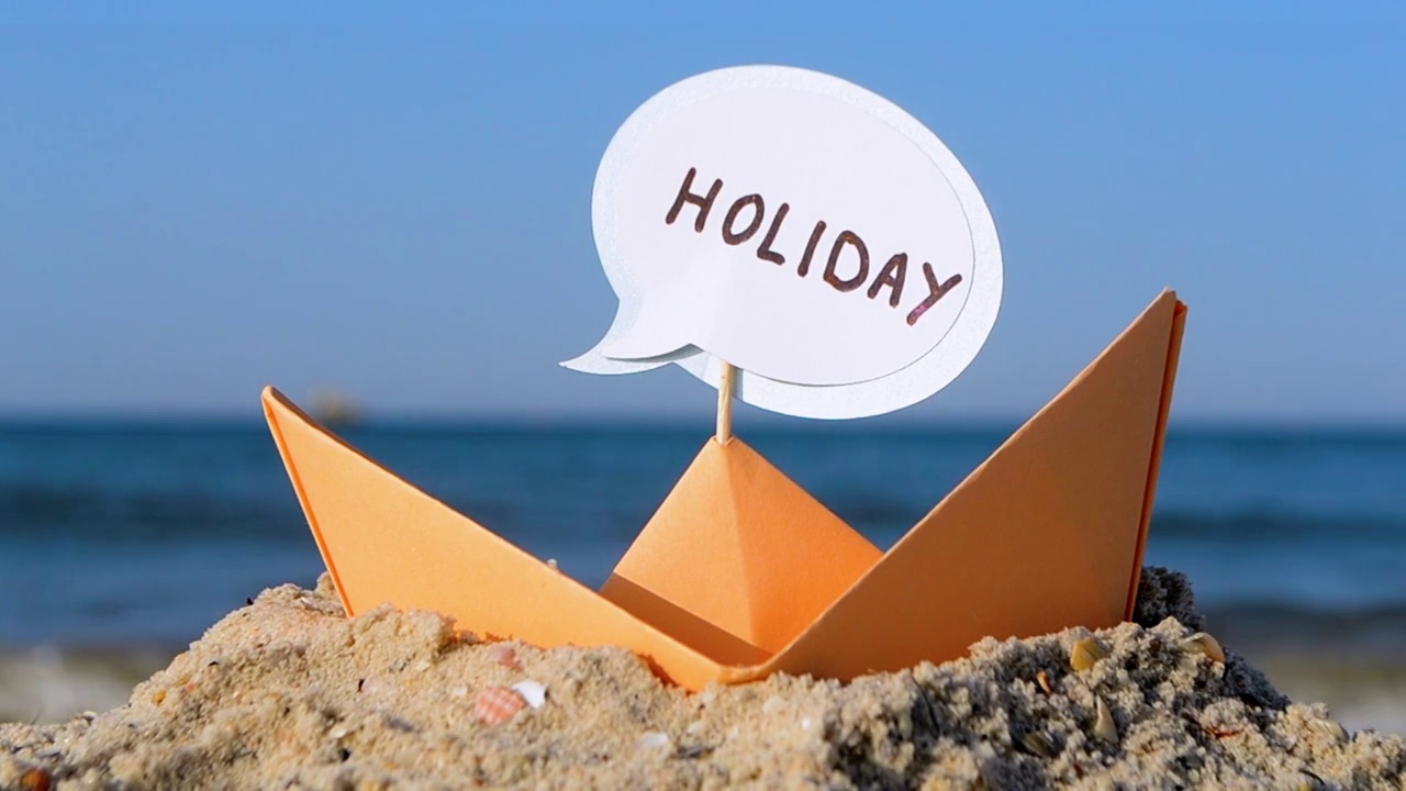 沙滩上的橙色纸船特写。阳光明媚的夏日，蓝色大海背景纸上的小船。坚持把单词Holiday插入到Boat中。概念旅游，旅游，度假，休息视频下载