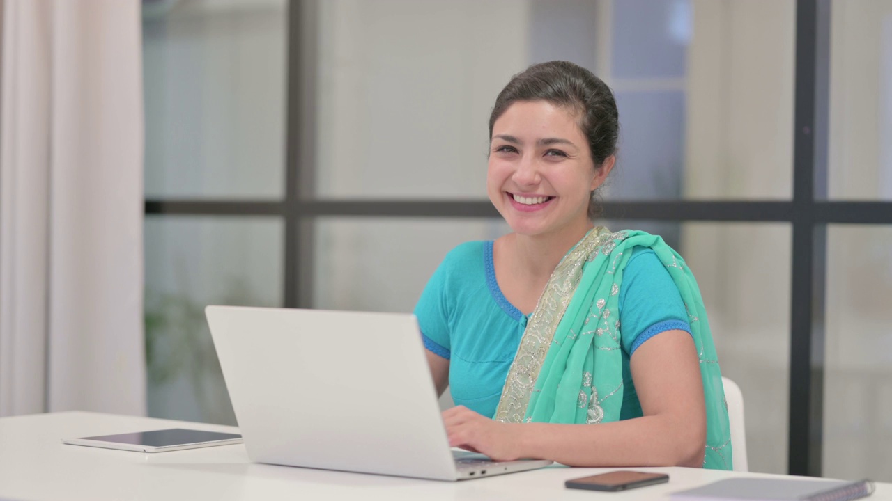 印度妇女在办公室使用笔记本电脑时对着镜头微笑视频素材