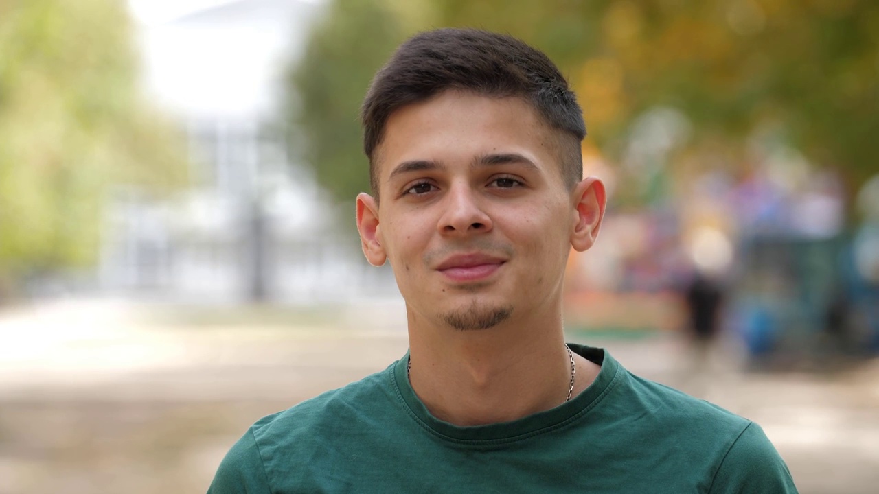 一个穿着绿色t恤的快乐的年轻人站在夏天的户外微笑视频素材