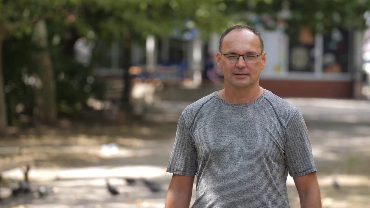 一个快乐的中年男人戴着眼镜，站在夏天的绿色公园里傻笑视频素材