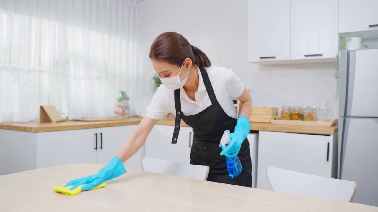 亚洲主动清洁服务女工清洁厨房和家庭。年轻漂亮的女管家清洁工戴上口罩，心情愉快地擦拭着脏乱的桌子，为家政做家务或杂务视频下载