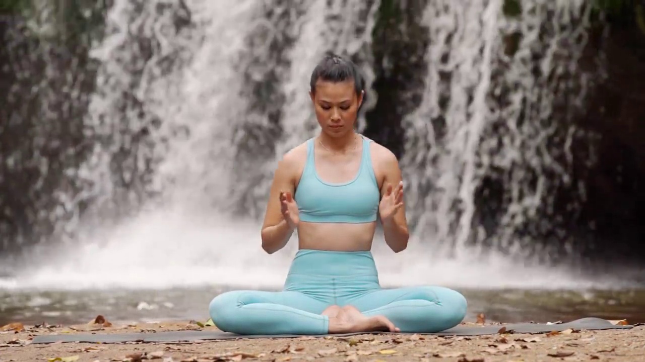 快乐女人瑜伽姿势平衡身体冥想在自然瀑布背景。视频下载