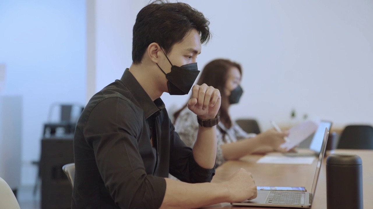 亚洲商人戴着口罩在笔记本电脑上工作视频素材