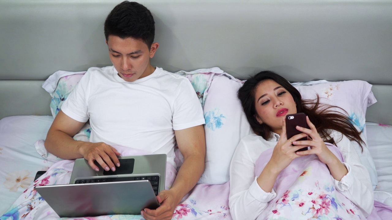 夫妇在床上使用笔记本电脑和智能手机视频素材