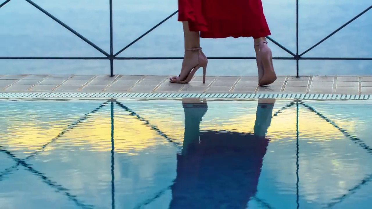 游泳池边漫步的女神。穿着红色庄严的连衣裙，贴近双腿视频下载