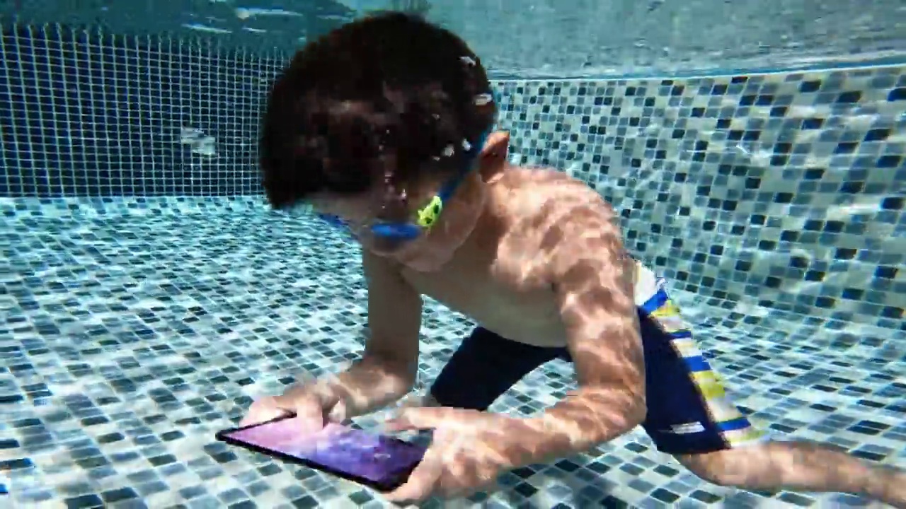 亚洲男孩在游泳池里用智能手机玩和游泳视频素材