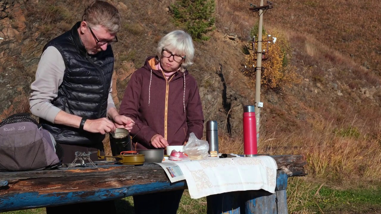 秋天在大自然中野餐。一个中年男人和一个中年女人站在一张木桌边吃着热汤面。4 k。视频下载