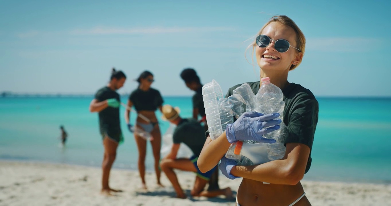 镜头中，戴着墨镜的金发女志愿者在海边捡起塑料垃圾，露出了满意的笑容。视频下载