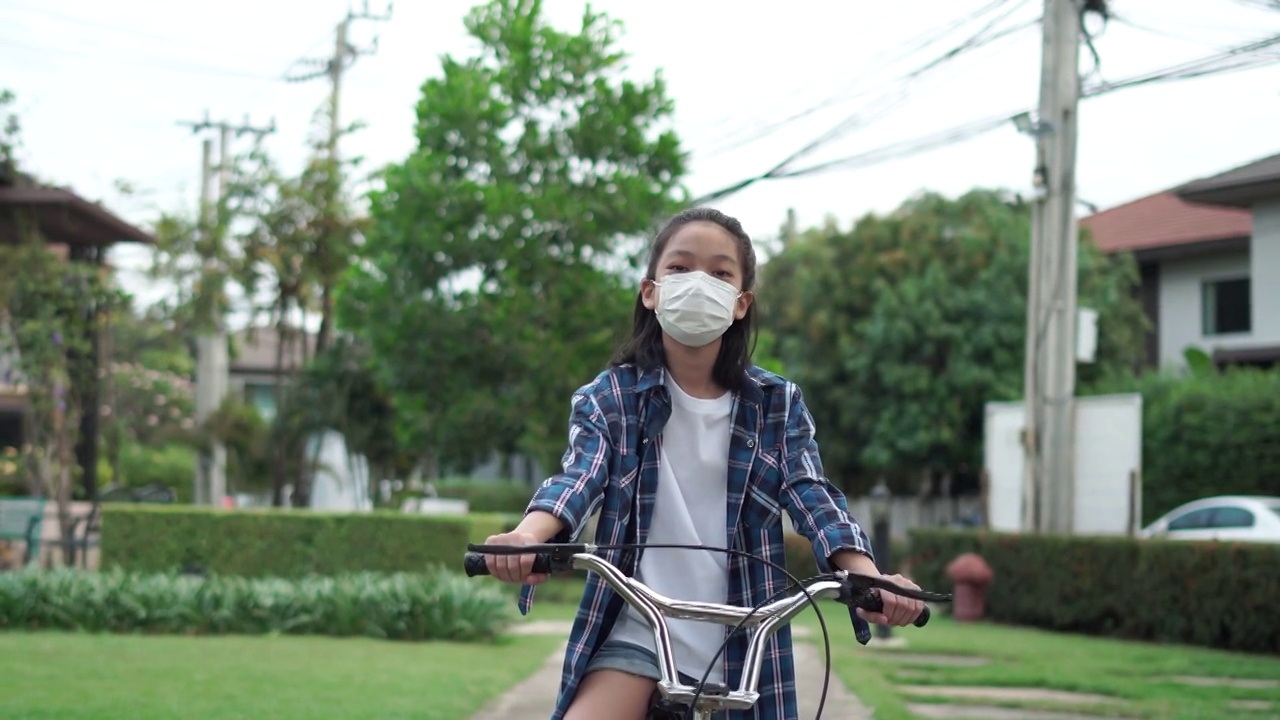 戴着防毒面具的小女孩坐在自行车上看着镜头，戴着防毒面具的小男孩微笑着骑在自行车上视频素材
