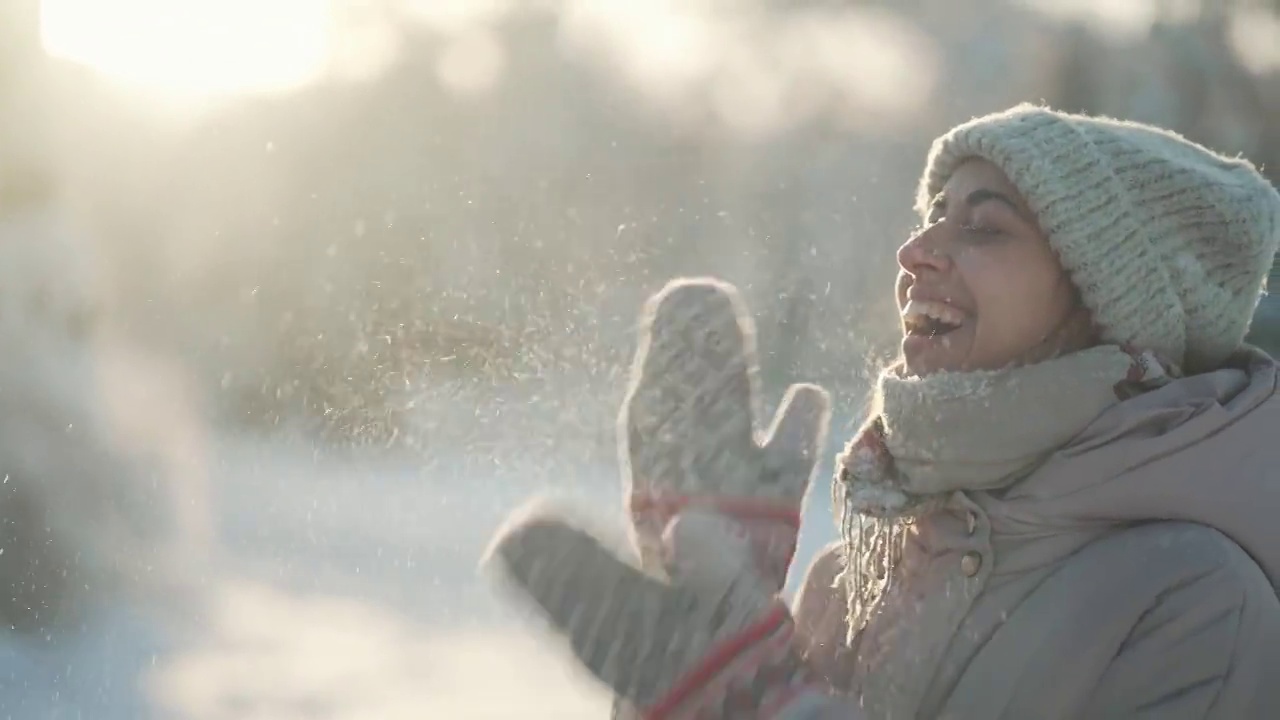 慢动作:年轻女子吹雪。在霜冻的冬日里，一个有趣的女孩在冬季公园里从手套里吹雪。快乐兴奋的女孩，享受着霜冻的新鲜，玩着新鲜的雪视频下载