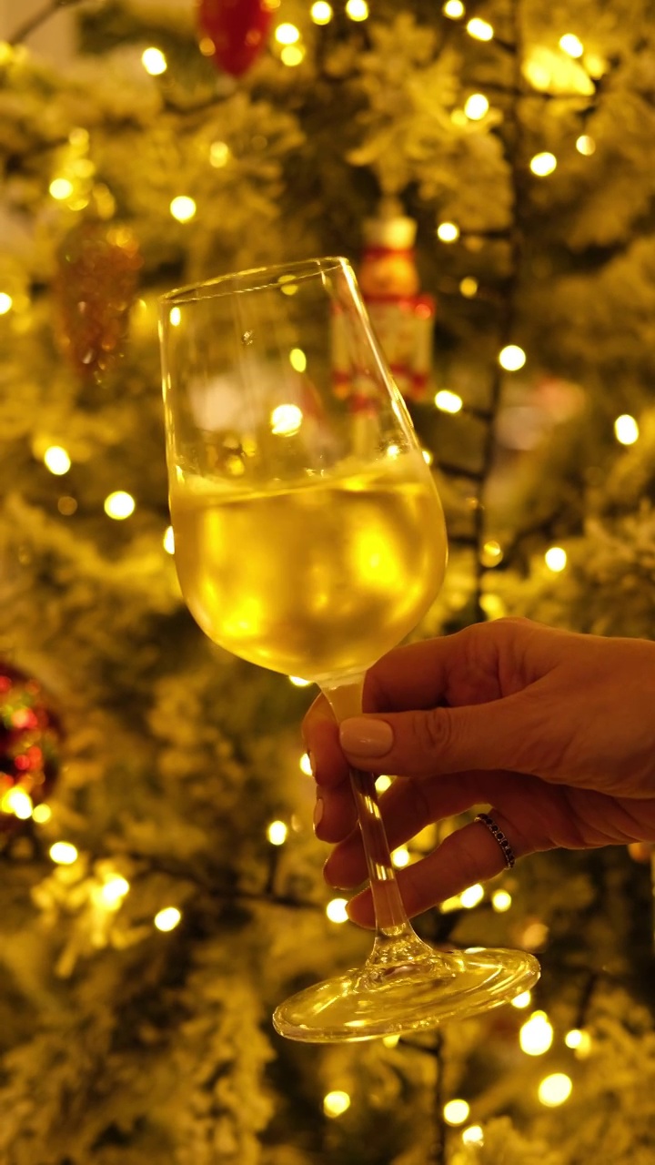 女人拿着一杯白葡萄酒，背景是圣诞彩灯。视频下载