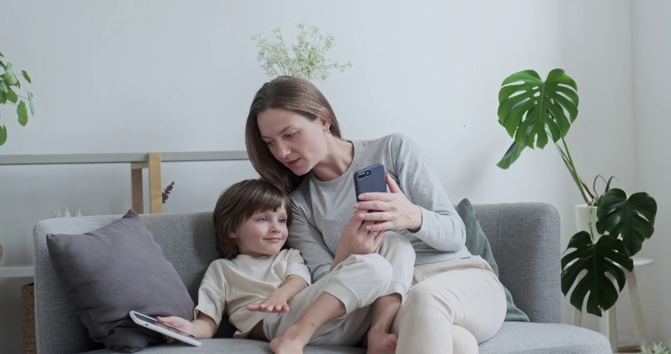微笑的母亲和小儿子摆姿势自拍，使用智能手机放松，享受家庭周末视频下载