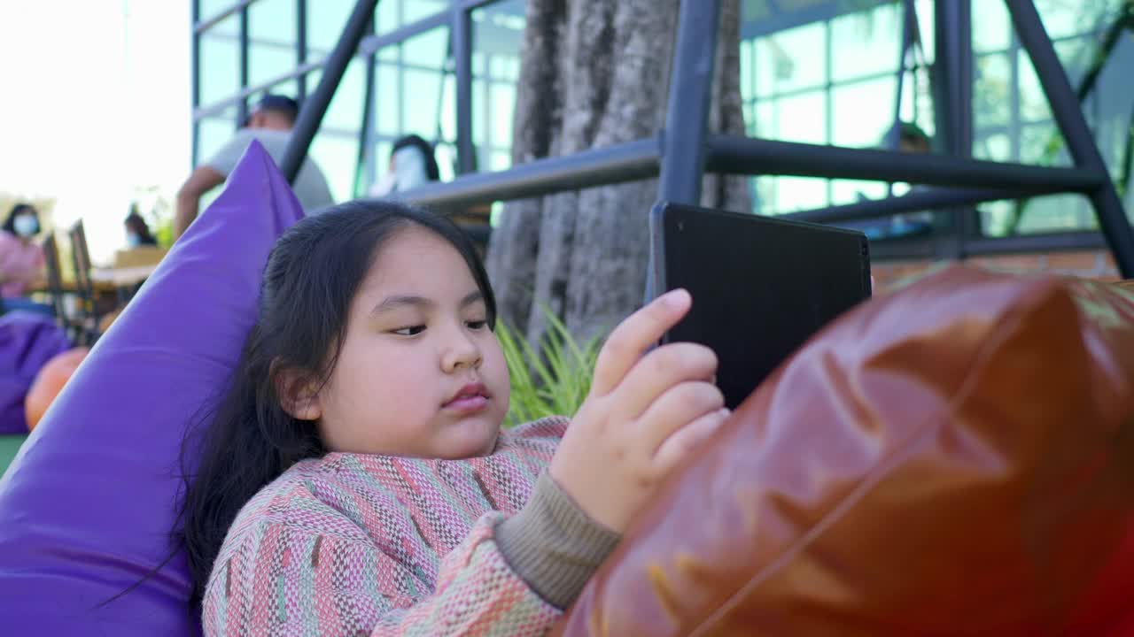 一个亚洲小女孩在公园里用平板电脑在线玩游戏视频素材