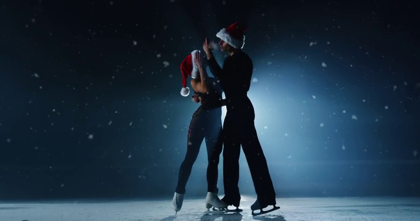 电影拍摄的一对花样滑冰选手戴着圣诞老人的帽子，在圣诞季节的比赛中表演一对花样滑冰舞蹈。假期概念，魔术，冬季运动。视频下载