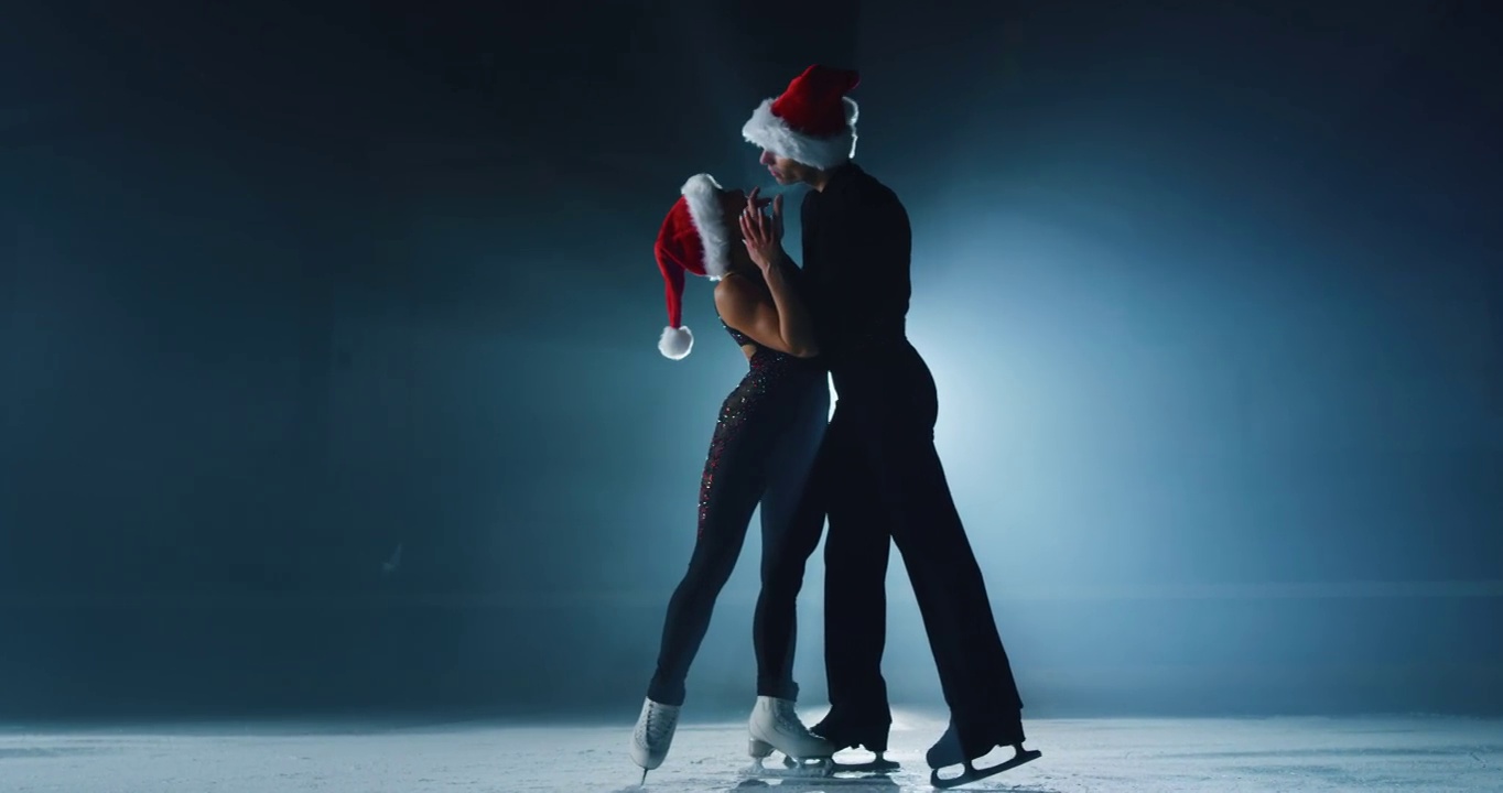 电影拍摄的一对花样滑冰选手戴着圣诞老人的帽子，在圣诞季节的比赛中表演一对花样滑冰舞蹈。假期概念，魔术，冬季运动。视频素材