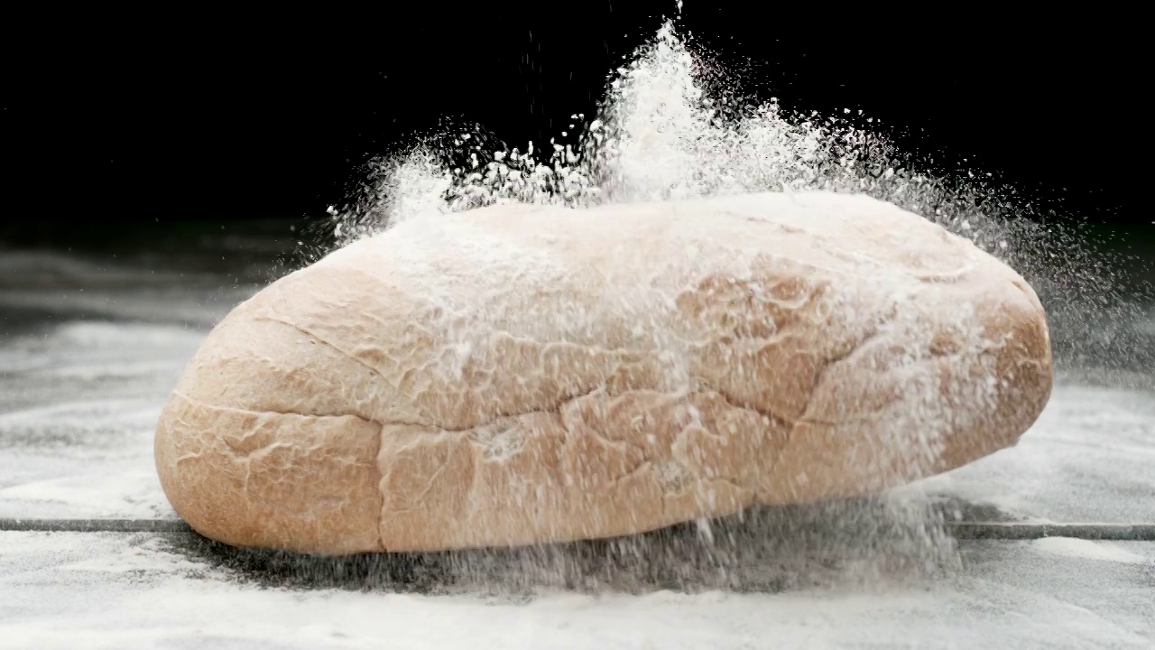慢镜头:面包掉在黑色表面的面粉上视频下载