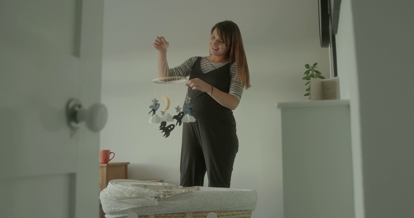 年轻孕妇用床上方悬挂的移动设备装饰房视频下载