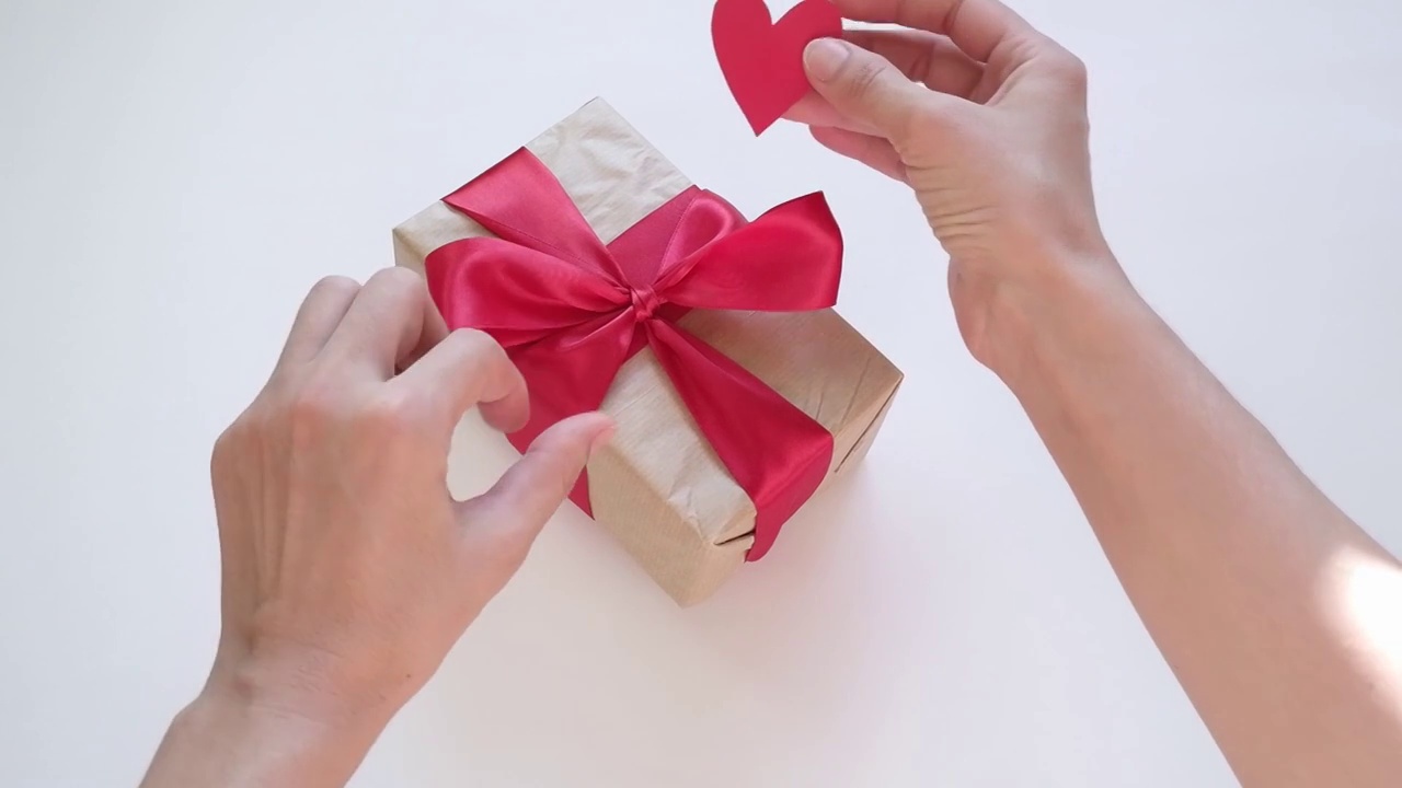 女性的手的特写放在桌子上的一个盒子与缎子红色的丝带，礼物和情人节卡片在一个心形视频下载