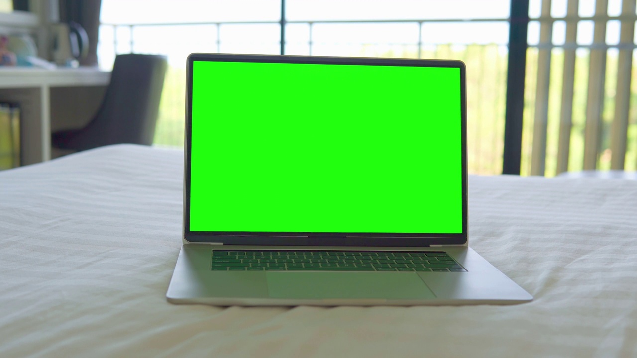 在家里的床上放一台带有绿色屏幕的笔记本电脑。视频下载