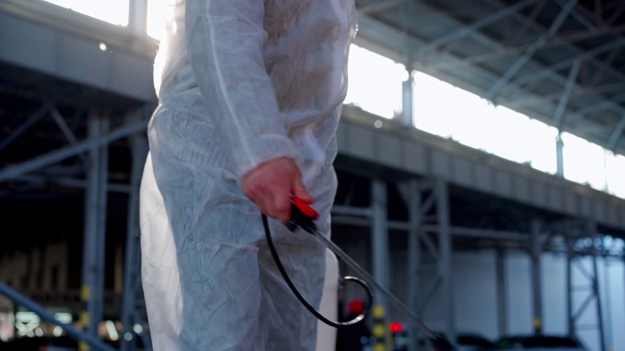 隔离期间，身穿白色防护服的男子在喷洒表面抗菌消毒液喷雾器视频素材