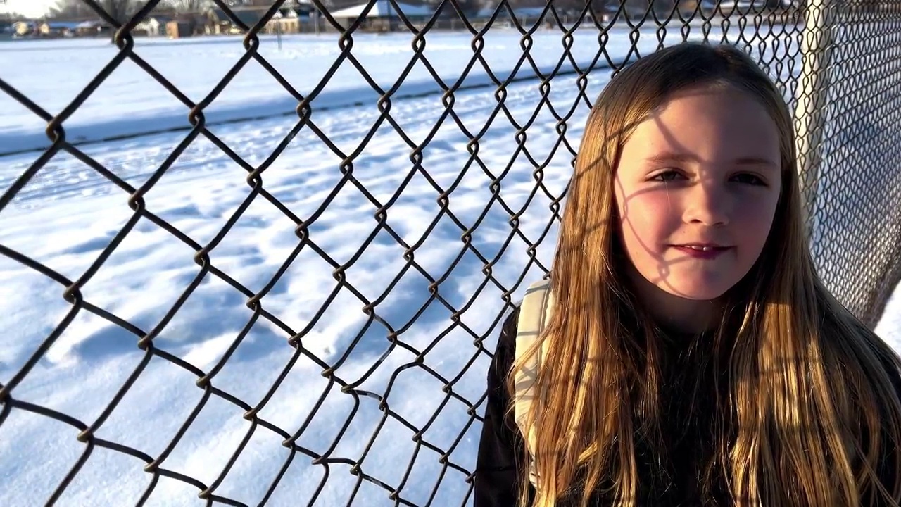 美丽的年轻女孩靠在铁链围栏，她身后的地面上的雪视频下载