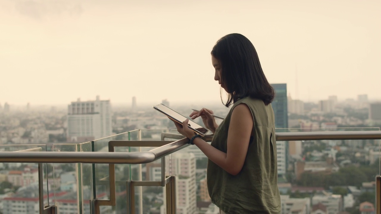 一位亚洲妇女在日落时分站在屋顶上使用平板电脑。视频素材