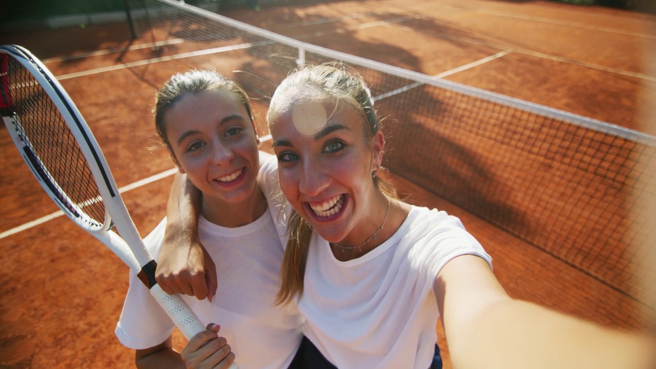 在一个阳光明媚的日子里，年轻快乐的青少年网球运动员朋友们在友谊赛或训练训练比赛结束后，在球场上愉快地与朋友或家人自拍或视频通话。视频下载