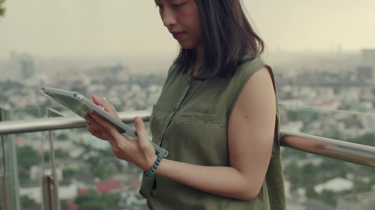 女性可以站在屋顶的阳台边用平板电脑和朋友聊天。视频素材