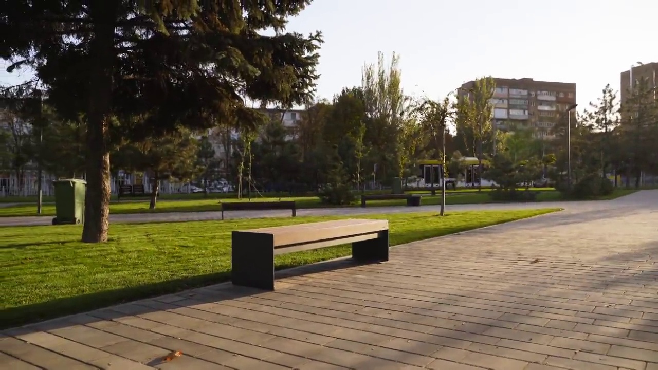公园草坪上的现代木凳。时尚的新长椅在城市休闲区日出或日落。城市主义主题公共空间景观设计。空旷的街道人行道上没有人视频素材