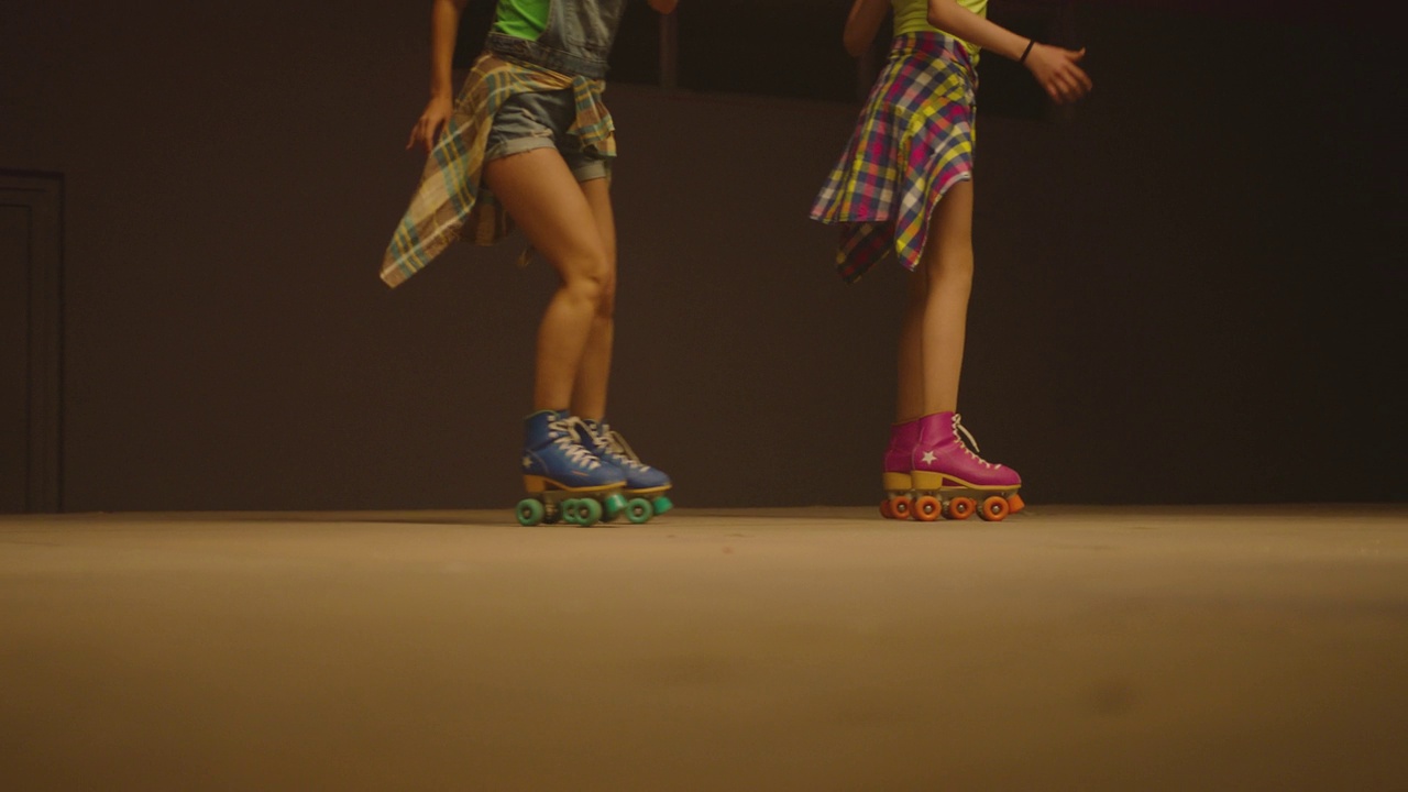 女人们穿着旱冰鞋，在旱冰场的地板上飞快地滑冰。年轻女子的腿部特写是专业滑冰。颜色各异的老式轮滑鞋。慢动作视频下载