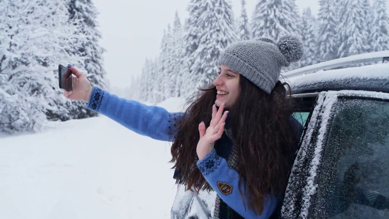 年轻女子在下雪天从车窗里用智能手机。视频下载