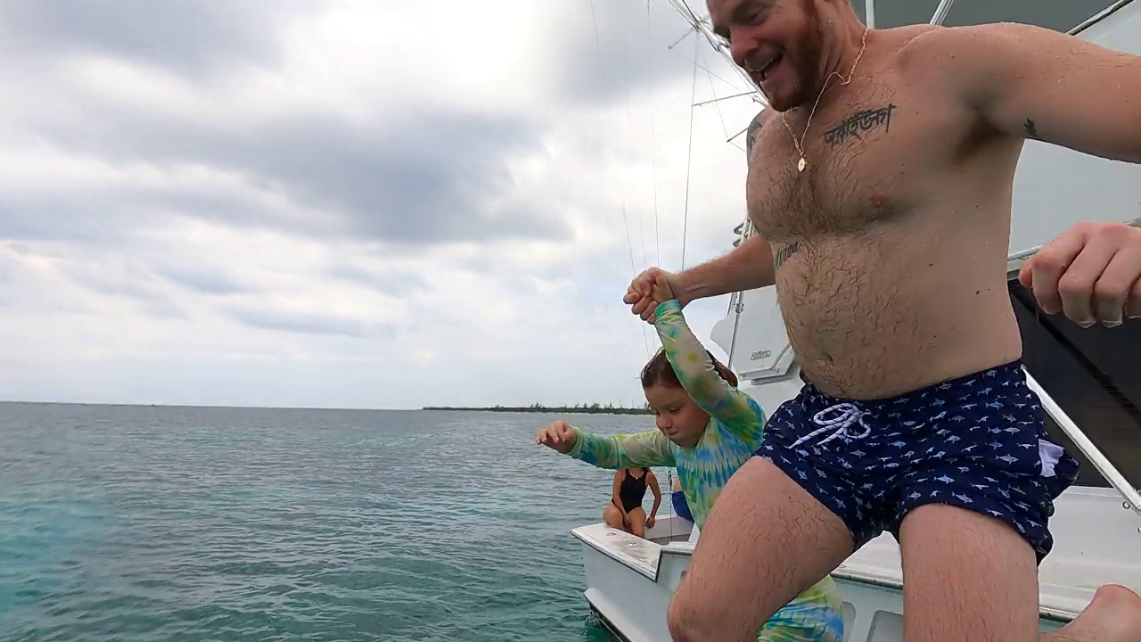 中宽镜头，父女俩手牵着手，从船边跳入热带海域视频下载