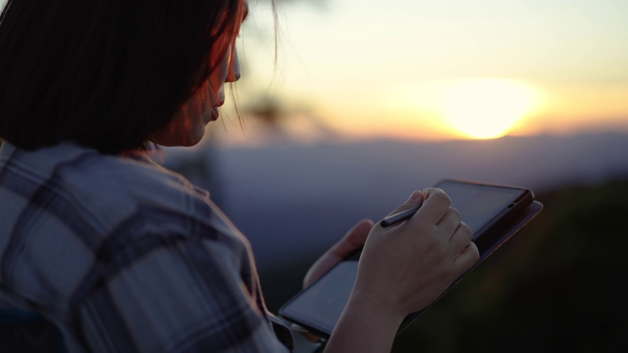 女人用她的平板电脑在放松的时间与日落在自然中视频下载
