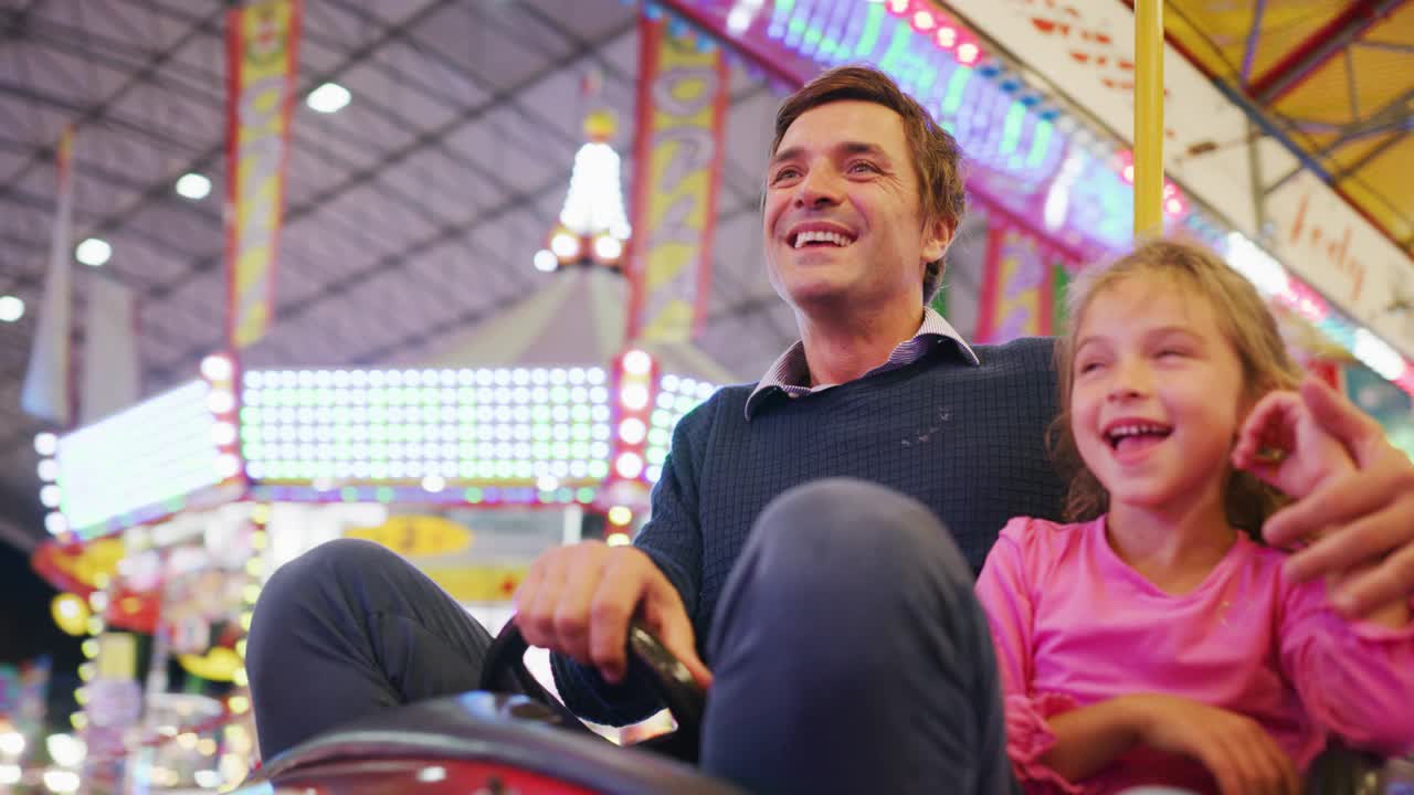 真实的照片，一个快乐的微笑的父亲和他的小女儿正在一起吃棉花糖的娱乐公园与月亮公园的灯在晚上。视频下载