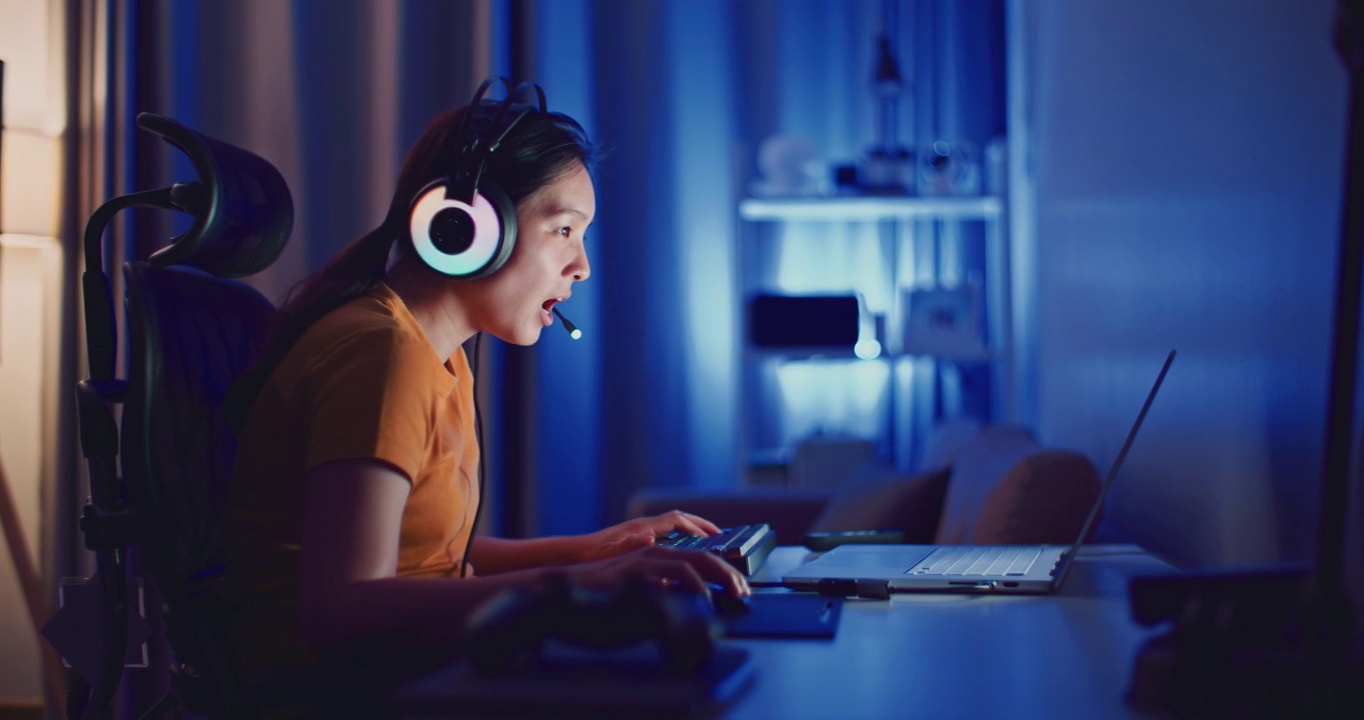 年轻的亚洲女性在晚上用笔记本电脑玩电脑游戏视频下载
