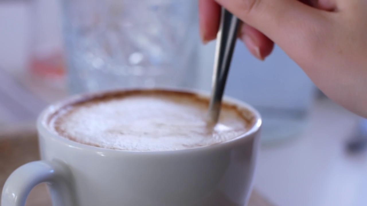 女士用勺子搅拌盛在玻璃杯里的厚泡沫的卡布奇诺咖啡。视频素材