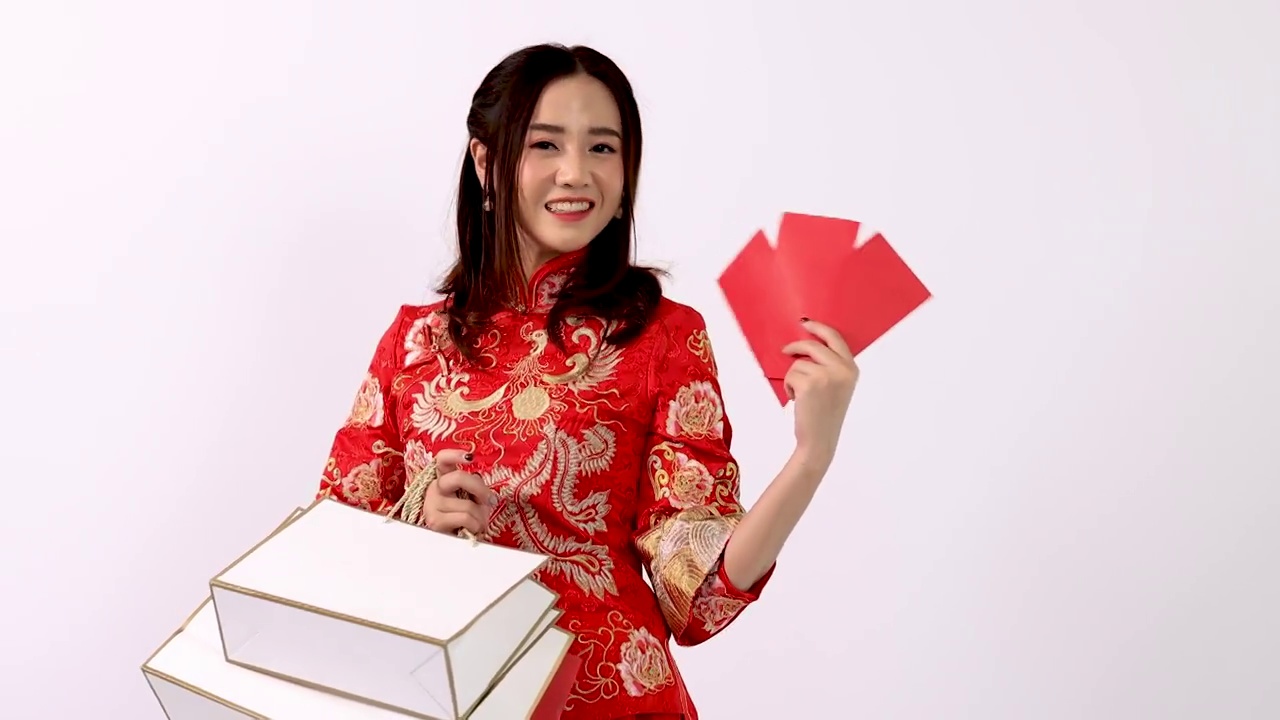 年轻女性亚洲妇女穿着红色旗袍服装展示红色昂宝和购物袋，中国新年视频下载