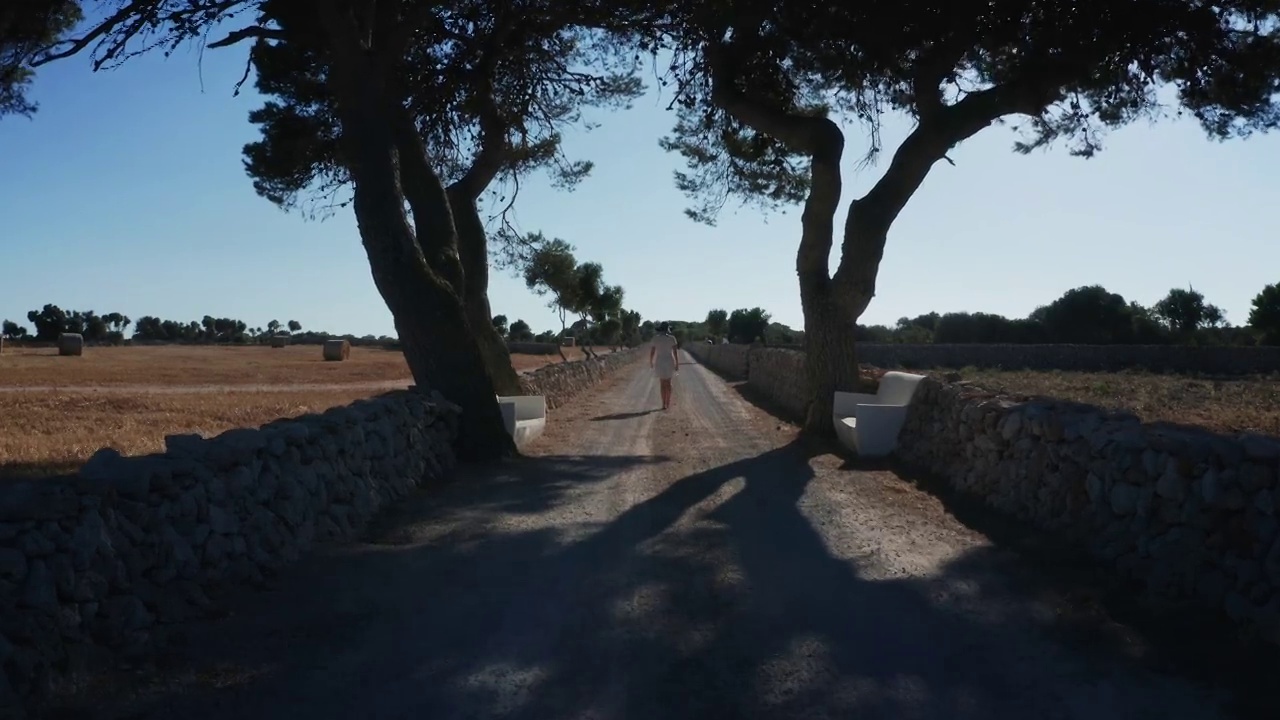 鸟瞰图从后面的一个年轻美丽的模特走在梅诺卡的乡间小路-西班牙4K视频下载