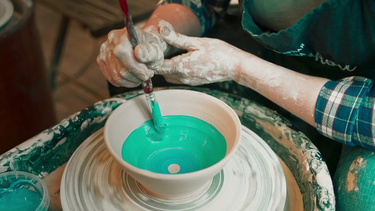 一个年轻女人的手用陶轮做陶器，在现成的碗上涂上釉。视频下载