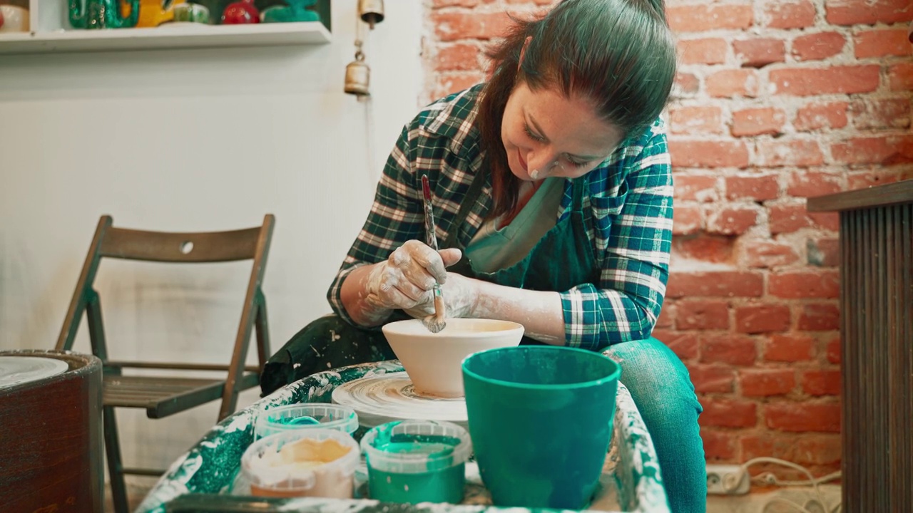 年轻女子正在用陶轮做陶器，给现成的碗上釉。视频下载
