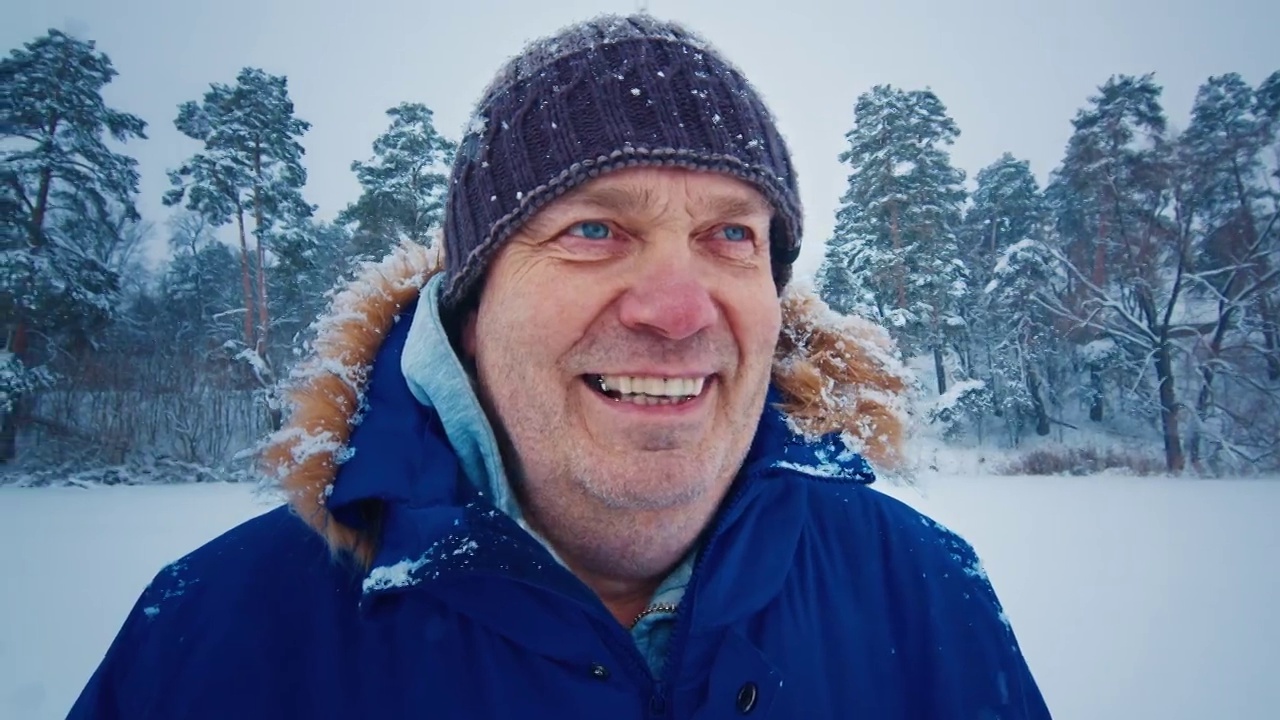 冬季户外肖像。老人站在雪地上看着相机的照片视频素材