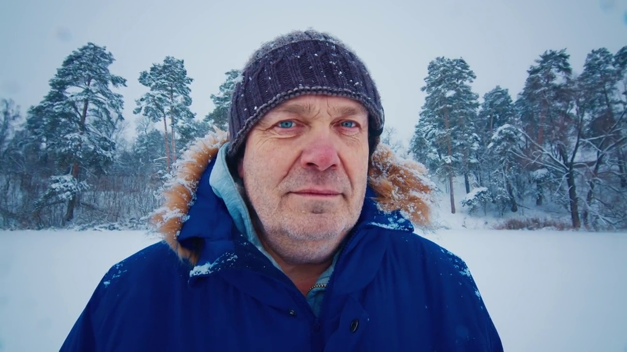 冬季户外肖像。老人站在雪地上看着相机的照片视频素材