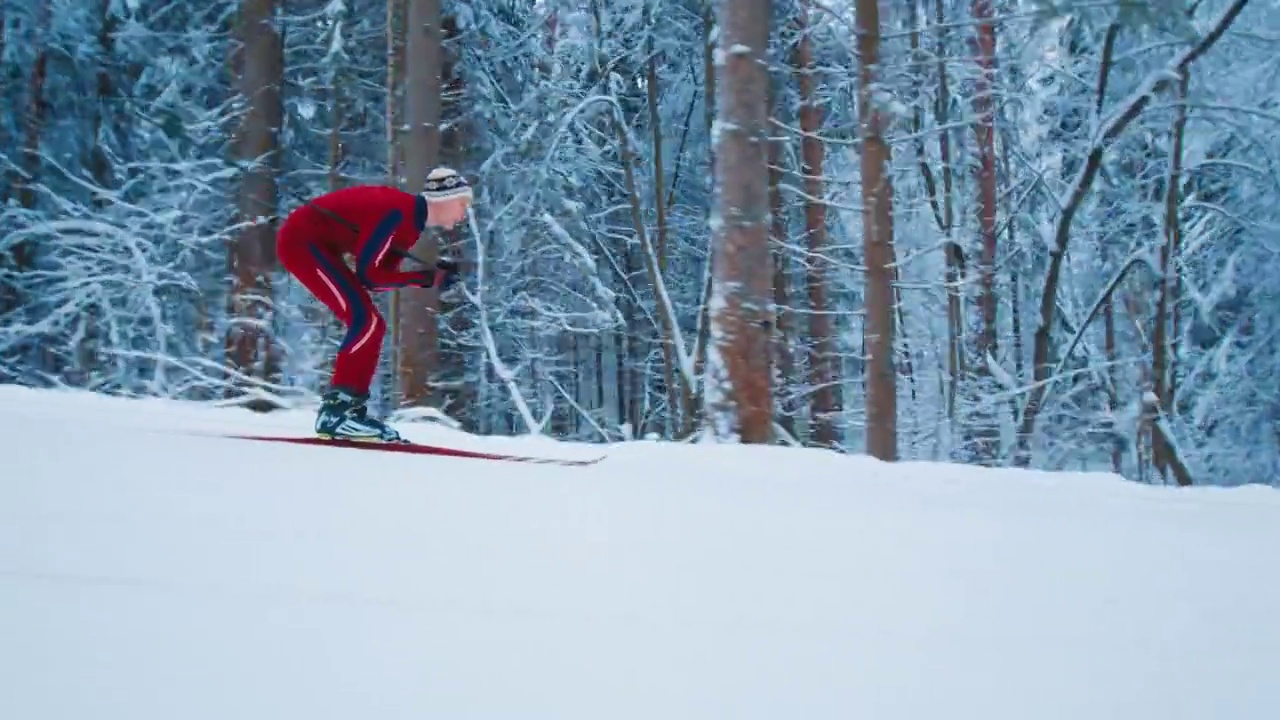 越野滑雪。穿着红色滑雪服的年轻男子在冬季森林滑雪视频下载