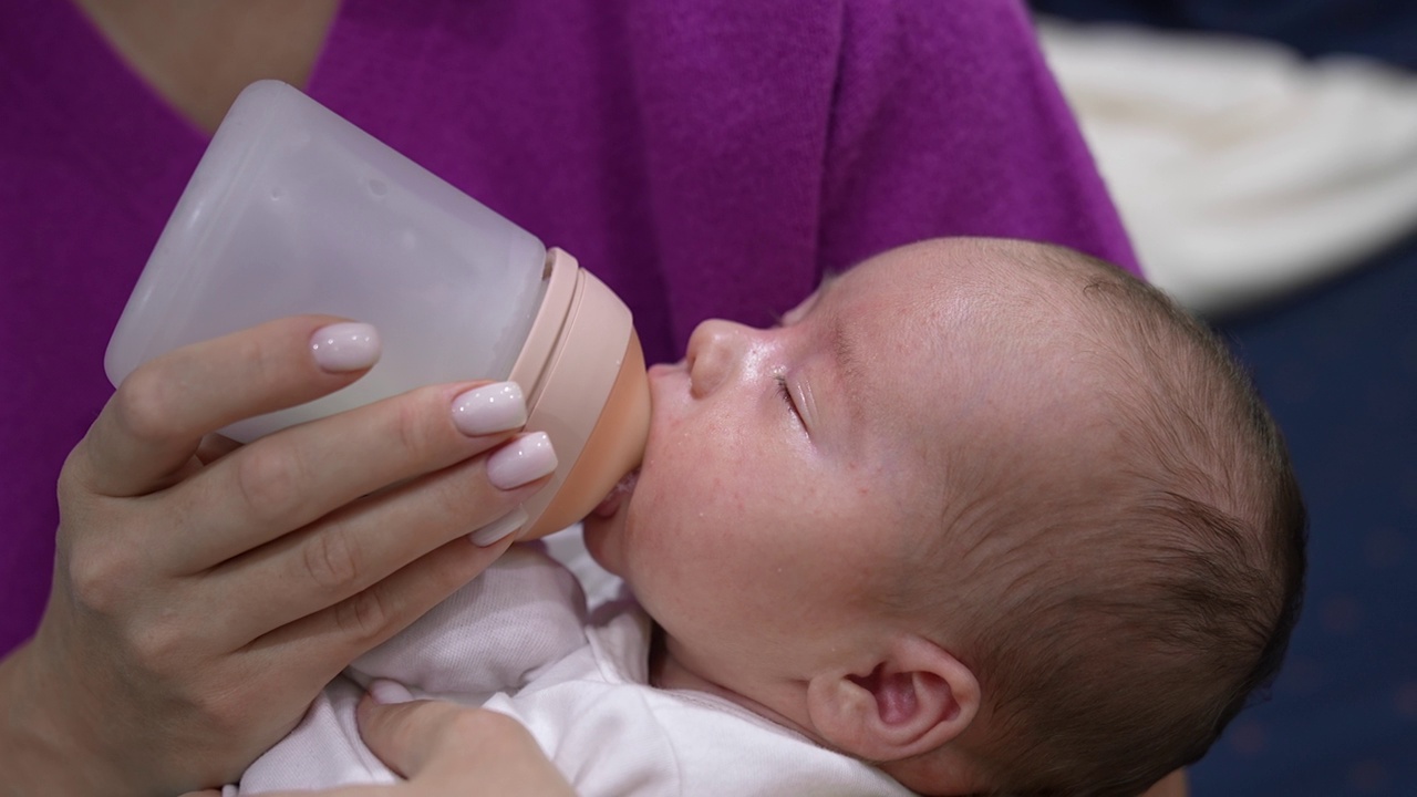 慈爱的母亲抱着一个婴儿，用奶瓶喂他。用奶瓶喂新生儿。关闭了。视频素材
