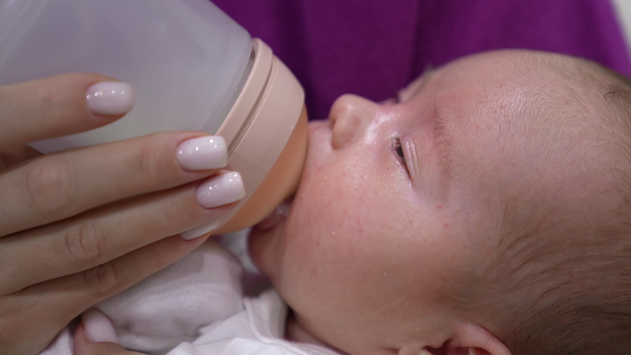 可爱的宝宝从奶瓶里吸着奶，慢慢地闭上眼睛。母亲的手拿着一个奶瓶给婴儿。可爱的婴儿脸靠近。视频素材