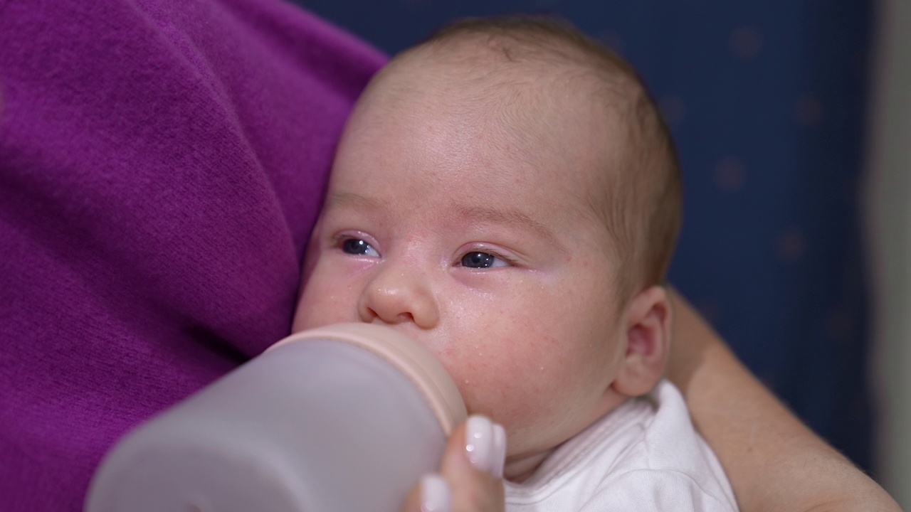 可爱的婴儿慢慢地从奶瓶里吸着奶。宝宝吃东西时闭上眼睛睡着了。孩子在妈妈的手中，靠近。视频素材