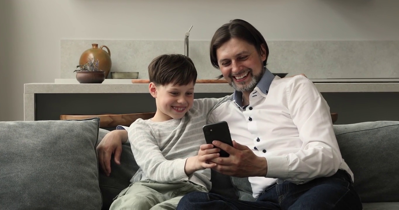 爸爸和8岁的儿子一起用智能手机坐在沙发上视频下载